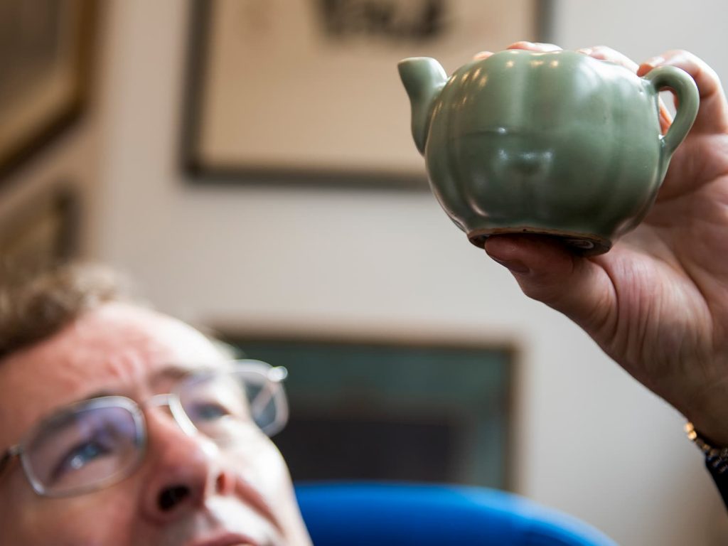 Person examining a small green ceramic teapot closely